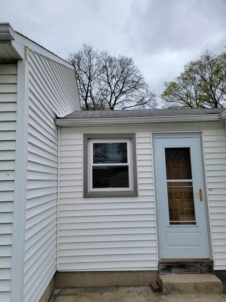side-door-and-window-exterior-renovation Home exterior with updated white siding, new window installation, and light blue side door.